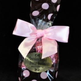 6 Pc Peanut Bruttle Bag.  Bruttles are wrapped in pink and brown foil and put into a brown cello bag with pink polka dots and closed with a pink satin ribbon.